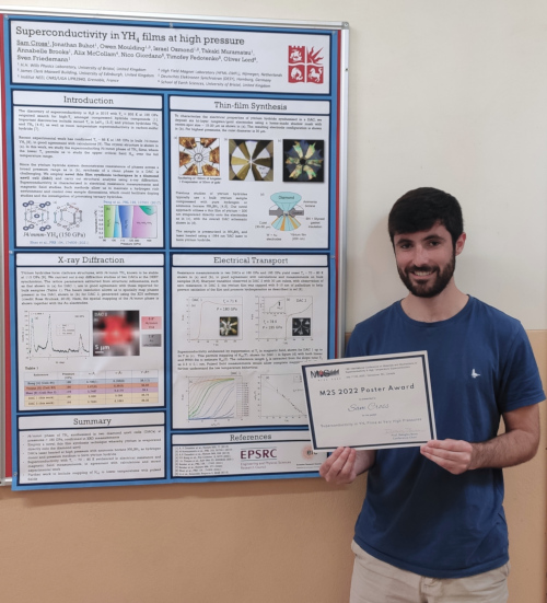 Sam Cross holds certificate awarded for winning the poster prize. They are stood in front of the poster